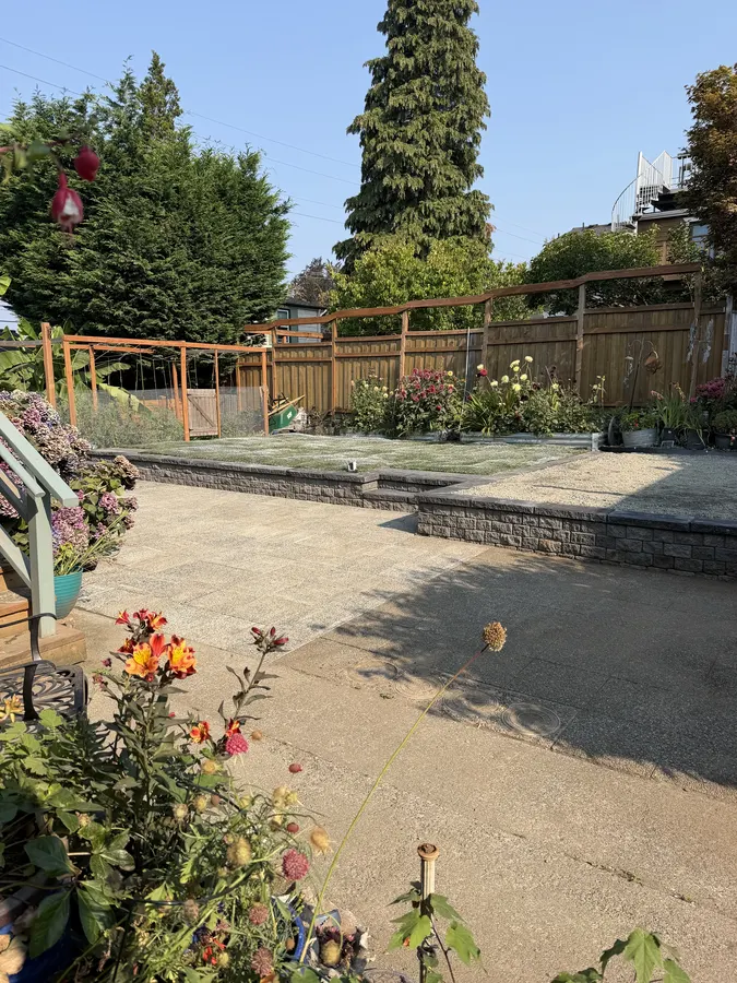 Finished paver patio with a low retaining wall, garden beds, and lawn